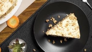 a slice of a two-layered carrot walnut cake with white frosting on a white plate