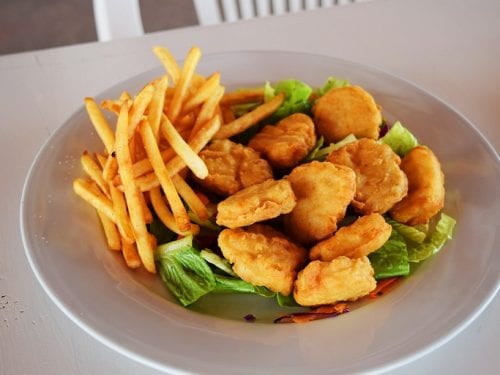 fried nuggets on a bed of green lettuce and with a side of fries in a white plate