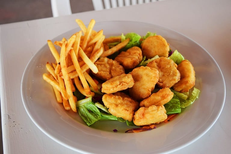 fried nuggets on a bed of green lettuce and with a side of fries in a white plate
