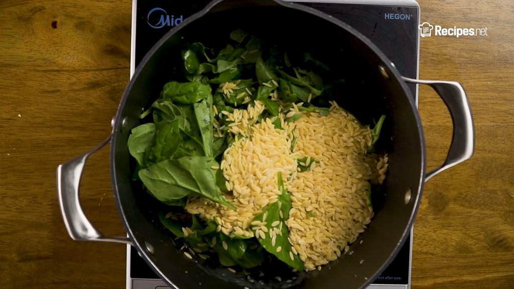 adding the spinach, pasta, chili flakes, and broth to the pan
