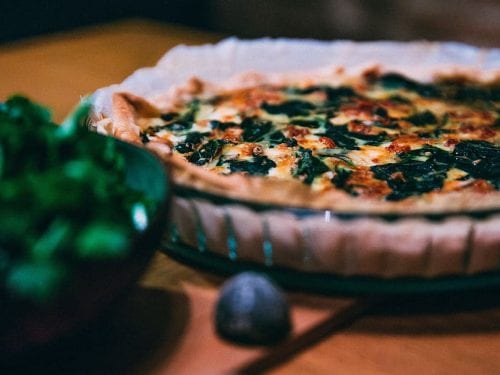 a spinach quiche in a baking dish with a bowl of spinach in the foreground