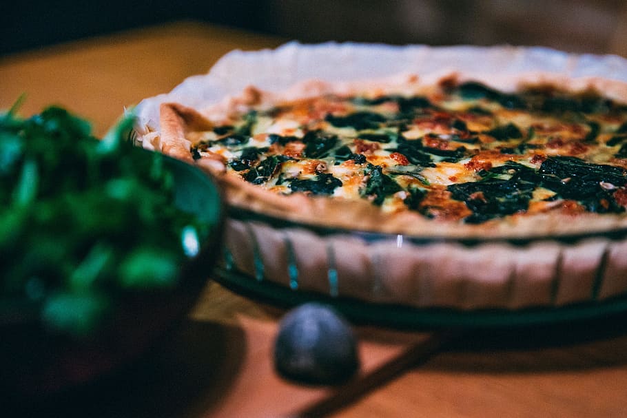 a spinach quiche in a baking dish with a bowl of spinach in the foreground