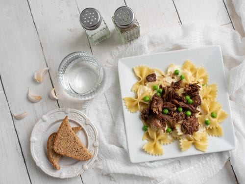 beef tips over garlic bowtie pasta with toasted bread nearby