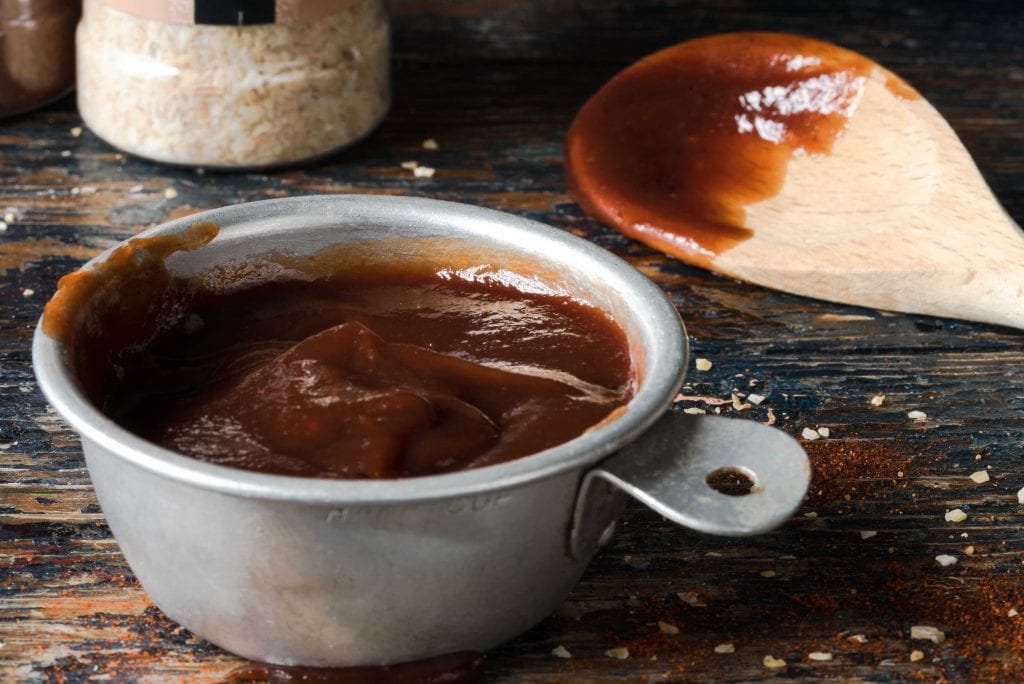barbecue sauce in a metal cup with a wooden spoon nearby