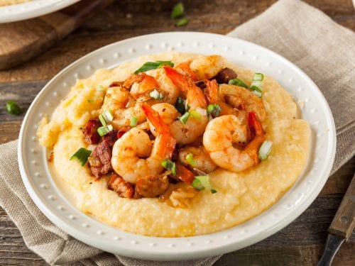 a white plate of shrimp and chunks of meat on grits