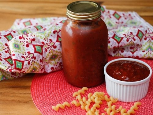Fresh tomato sauce in a bottle and a small bowl with scattered dry pasta around