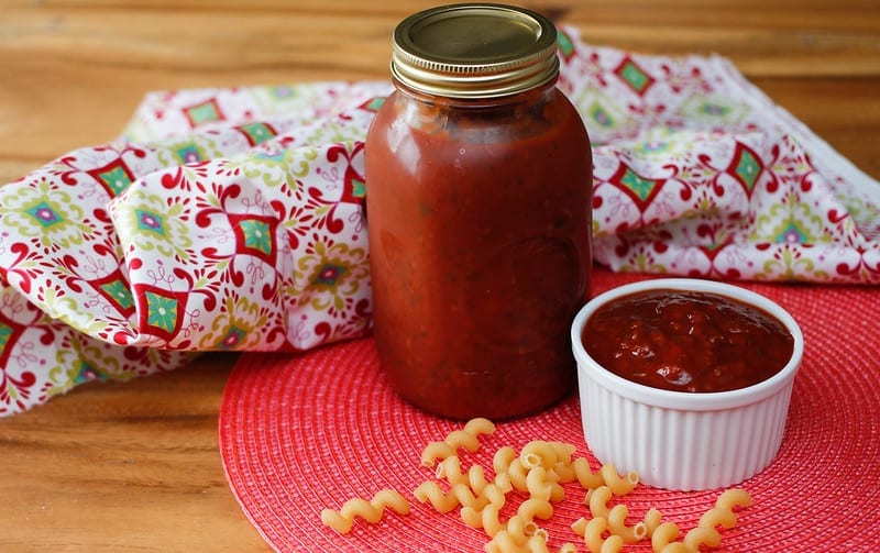 Fresh tomato sauce in a bottle and a small bowl with scattered dry pasta around
