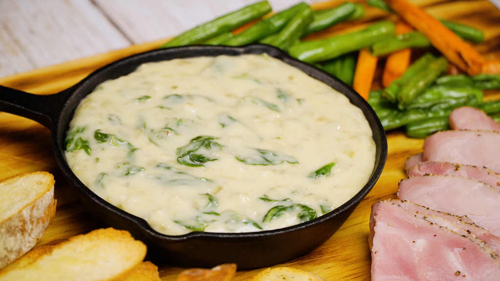 cheese fondue in a pot with bread, vegetables, and cold cuts on the side