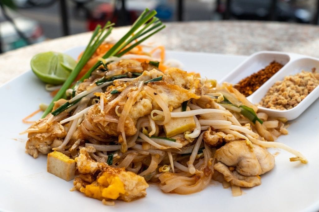 pad thai on a white plate with some garnishes on the side