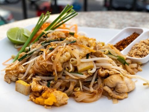 pad thai on a white plate with some garnishes on the side