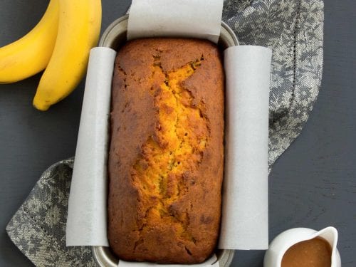 banana pumpkin bread with some bananas and a small jug of glaze nearby