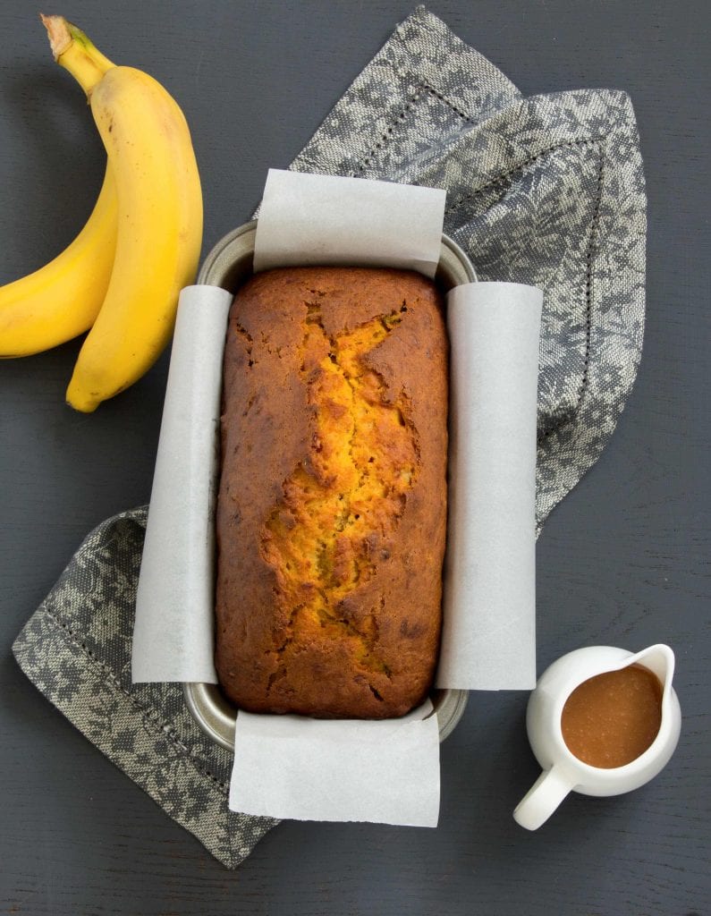 banana pumpkin bread with some bananas and a small jug of glaze nearby