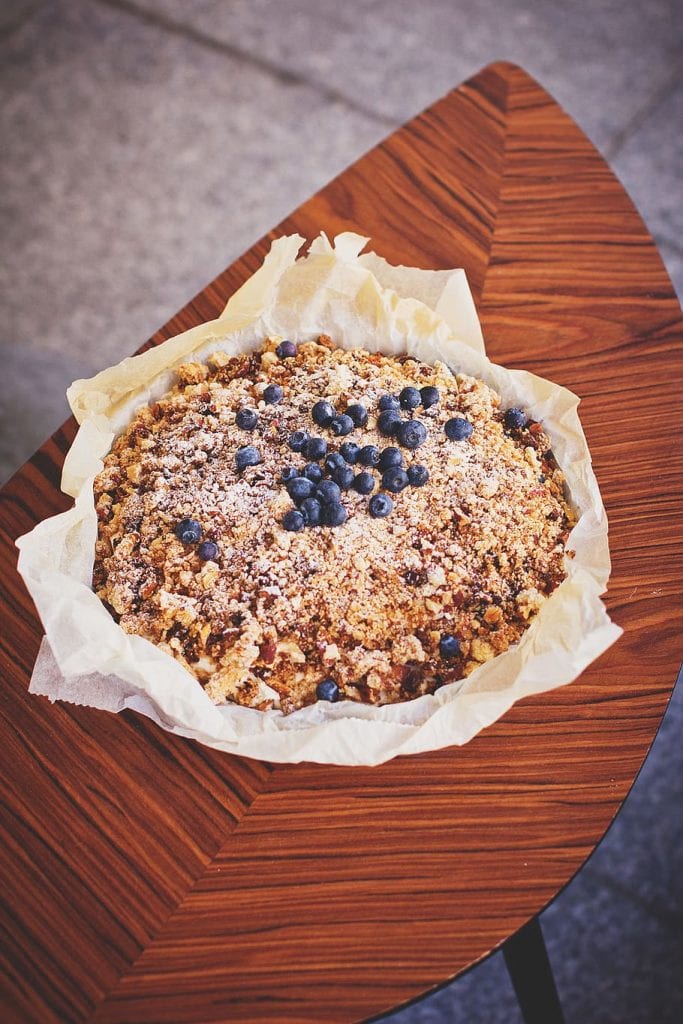 blueberry crumble pie topped with blueberries on a small wooden table