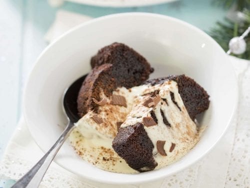 pieces of a chocolate bundt cake covered in cream in a white bowl
