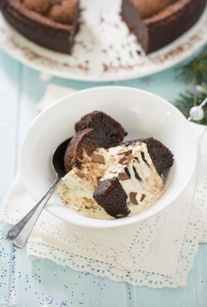 pieces of a chocolate bundt cake covered in cream in a white bowl