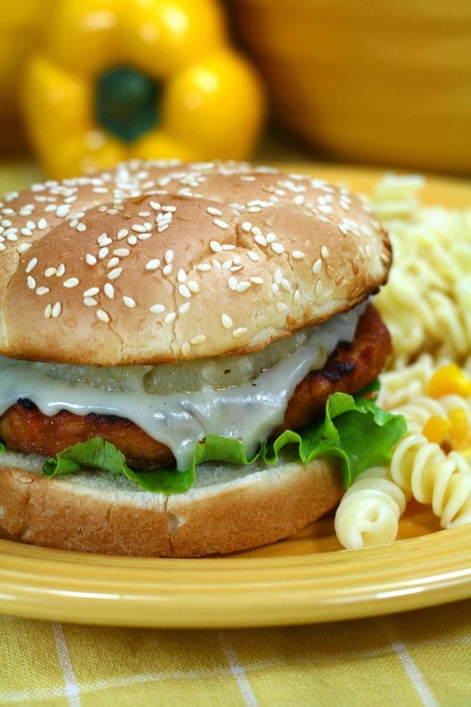 chicken burger with lettuce, cheese and pineapple on a yellow plate with pasta on the side