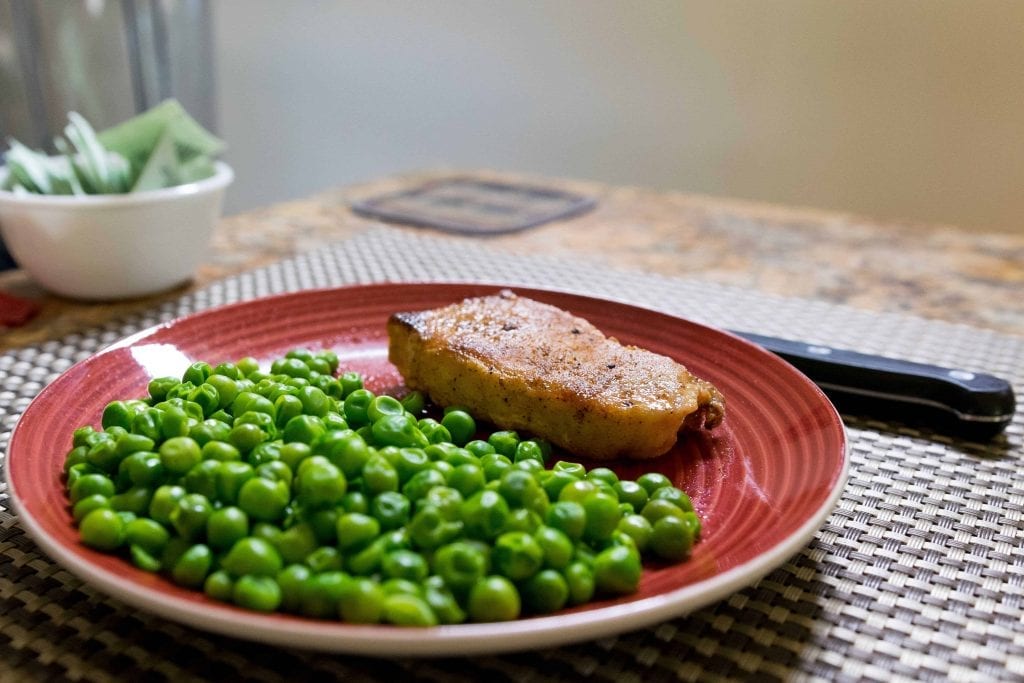 a slab of pork chop and peas on a red plate