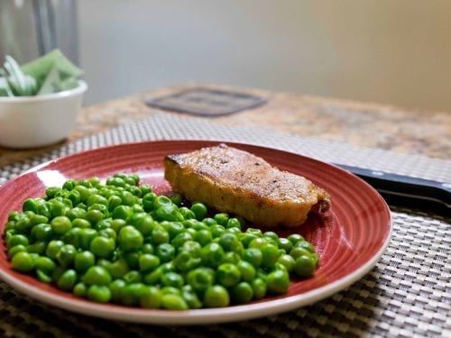 a slab of pork chop and peas on a red plate