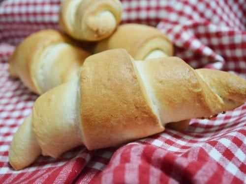 several crescent rolls in a basket lined with a red and white checkered cloth