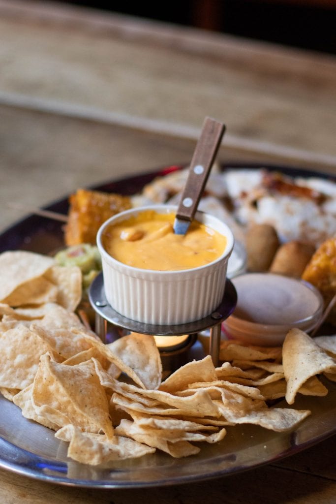 a small bowl of nacho cheese sauce surrounded by nacho chips and other finger foods