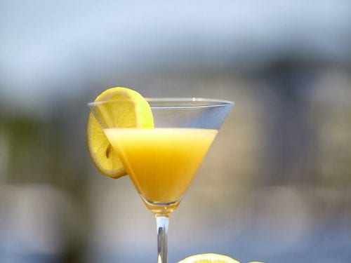 a bright yellow tropical cocktail in a martini glass garnished with a lemon slice