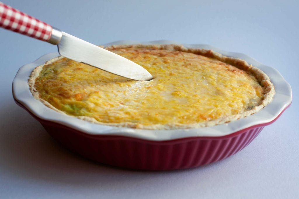 cheese-covered pie in a baking dish with a knife cutting into it