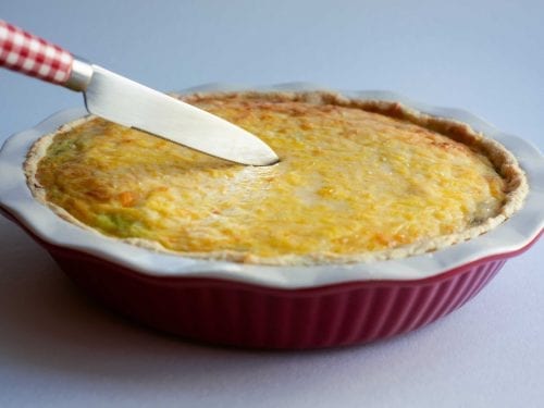 cheese-covered pie in a baking dish with a knife cutting into it