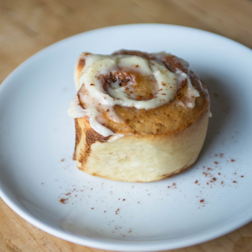 a single cinnamon roll with icing on a white plate