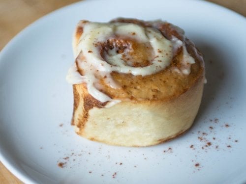 a single cinnamon roll with icing on a white plate