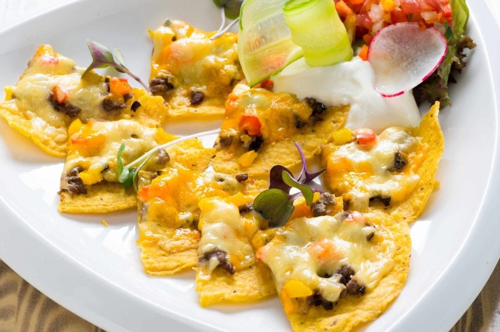 nacho chips on a white plate dipped in a cheesy meat sauce