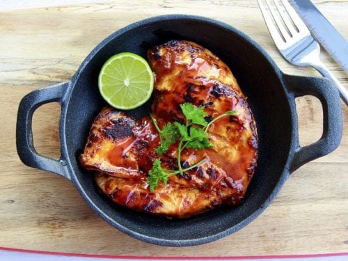 bbq chicken with half a lime and cilantro garnish in a black pan
