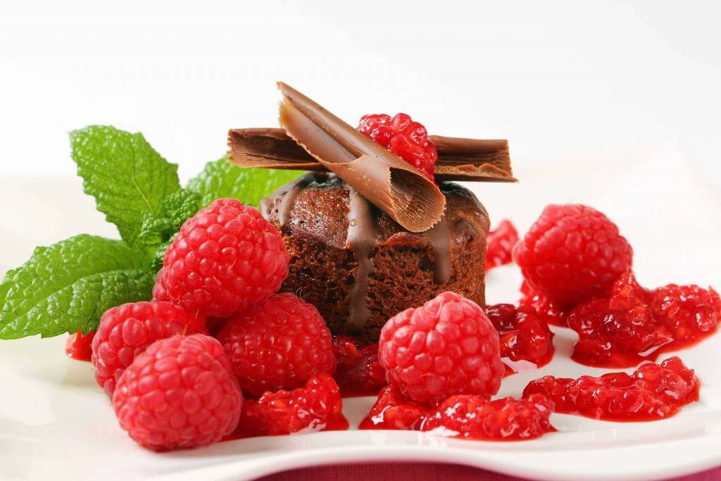 mini chocolate cake covered with raspberry coulis, raspberries, mint and chocolate pieces