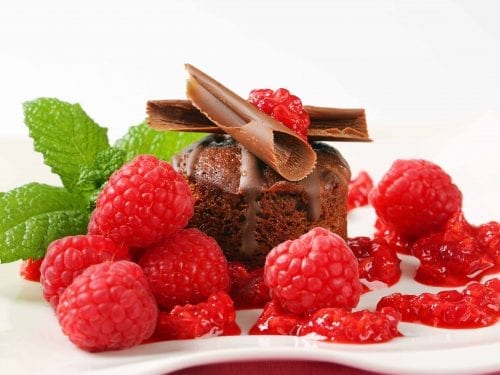 mini chocolate cake covered with raspberry coulis, raspberries, mint and chocolate pieces