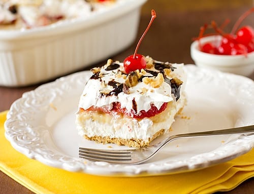 No-Bake Banana Split Cake Recipe, banana split cake with graham cracker crust, frosting, and cherries