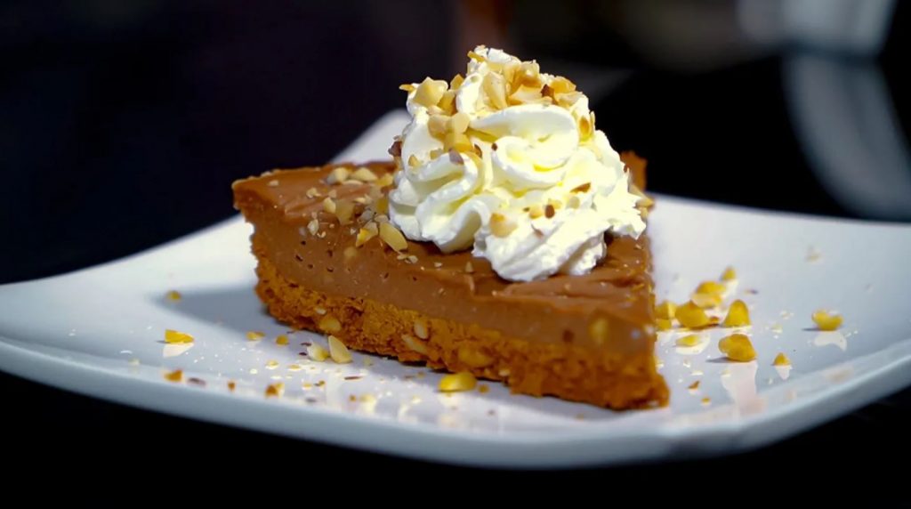 No Bake Nutella Cheesecake, Nutella cheesecake slice topped with chopped hazelnuts and whipped cream and served on a white plate