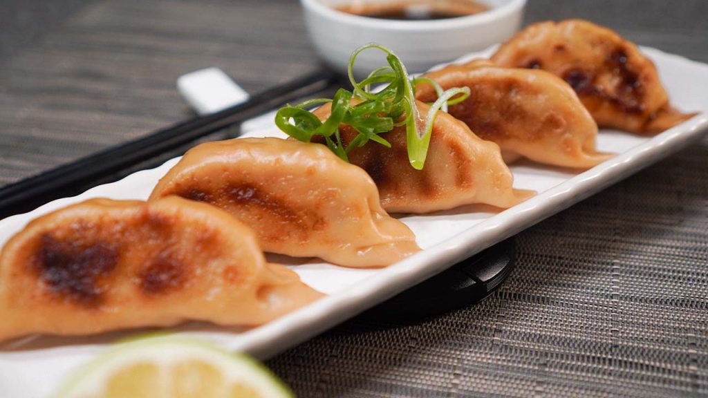 Copycat Cheesecake Factory Chicken Pot Stickers Recipe, Pot stickers lined up and served on a long white ceramic plate