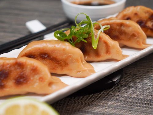 Copycat Cheesecake Factory Chicken Pot Stickers Recipe, Pot stickers lined up and served on a long white ceramic plate