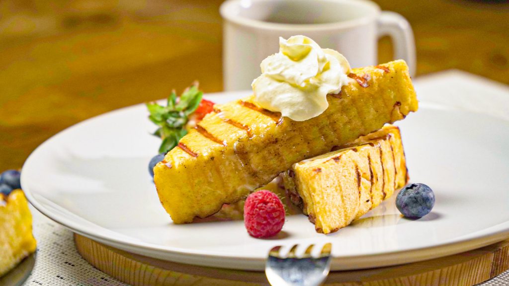 Eggnog French Toast Recipe, Two pieces of Eggnog French toast on a plate, topped with whipped cream and served with two berries on a white plate