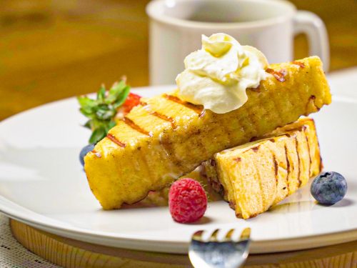 Eggnog French Toast Recipe, Two pieces of Eggnog French toast on a plate, topped with whipped cream and served with two berries on a white plate