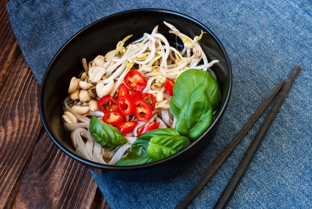 vegtarian pho garnished with nuts, red chilis, basil, and mung bean sprouts