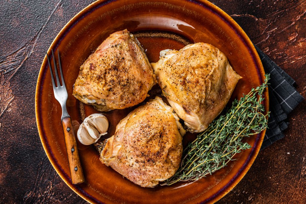 Roasted chicken thighs with spices in a plate. Dark background.