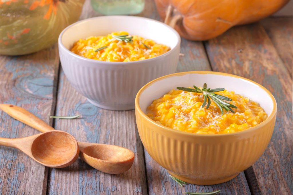 Two bowls of butternut pumpkin risotto with parmesan cheese on a wooden background.