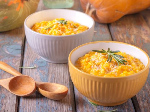 Two bowls of butternut pumpkin risotto with parmesan cheese on a wooden background.