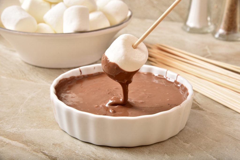 S'mores pops or marshmallow on a stick, dipped in a bowl of melted chocolate