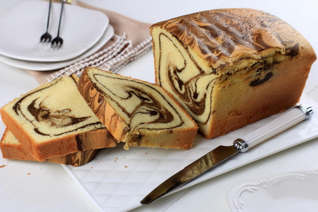 sliced loaf marble cake on white plate, wooden table homemade baked goods