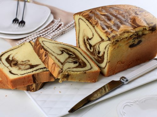 sliced loaf marble cake on white plate, wooden table homemade baked goods