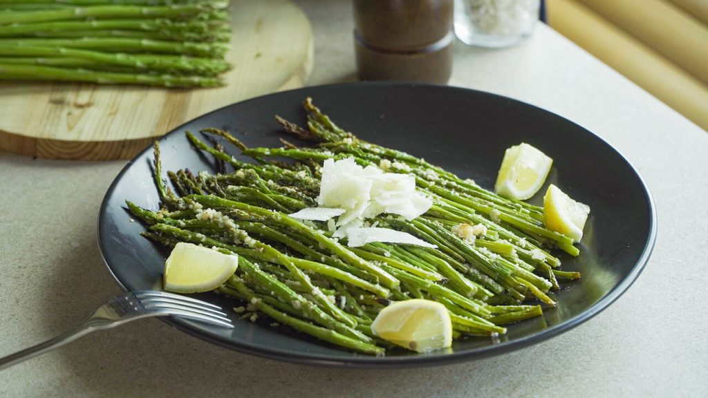 Roasted Parmesan Asparagus Recipe, Roasted asparagus tossed with grated parmesan and served with lemon wedges on a black plate