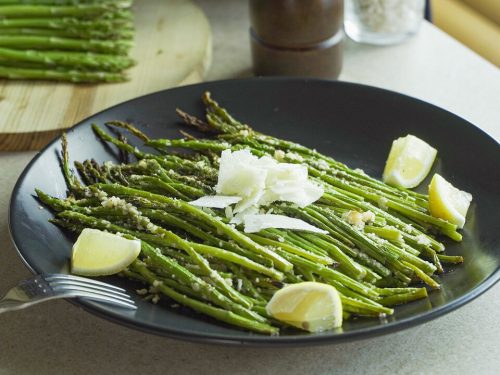 Roasted Parmesan Asparagus Recipe, Roasted asparagus tossed with grated parmesan and served with lemon wedges on a black plate
