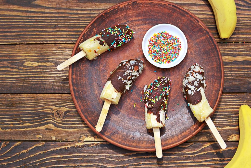 dessert, frozen bananas in chocolate on a stick on a brown clay plate, tropical desserts, party