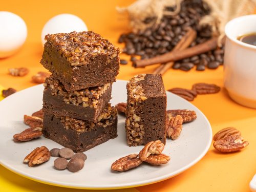 Pecan Pie Brownies Recipe, Pecan pie brownies cut into squares and served on top of a white plate decorated with pecans and chocolate chips